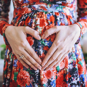 Schwangere formt mit Händen Herz auf Bauch