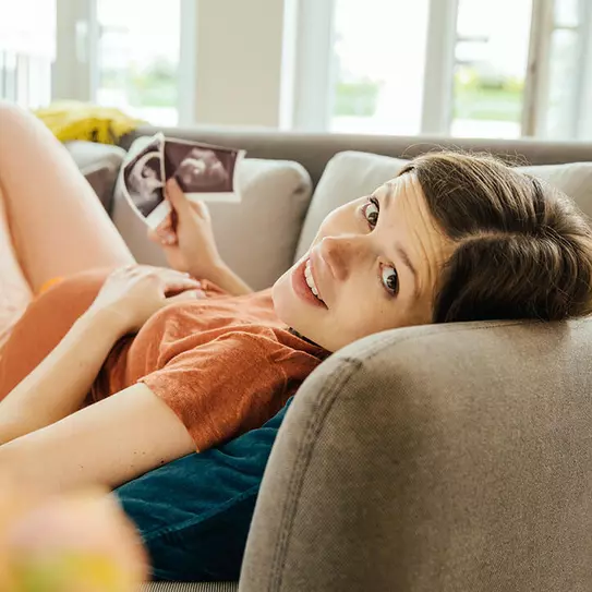 Schwangere Frau mit Ultraschallbildern liegt auf Sofa