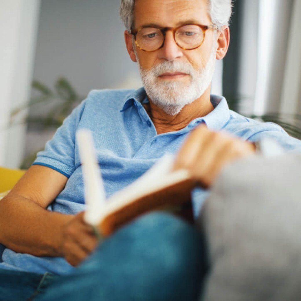 Älterer Herr liest ein Buch auf der Couch
