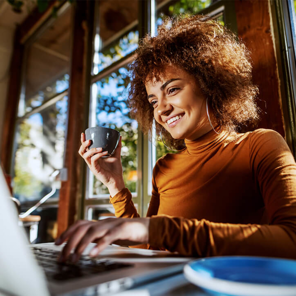 Frau mit Kaffeetasse vor dem Laptop im Büro