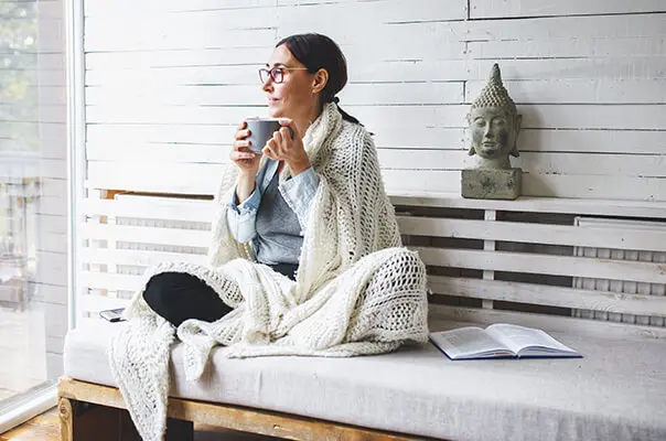 Frau sitzt mit Tee und Decke in Wintergarten