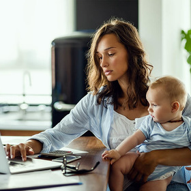 Frau mit Baby auf dem Schoß arbeitet am Laptop