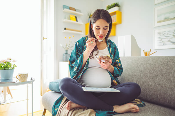 Schwangere Frau isst Müsli auf dem Sofa