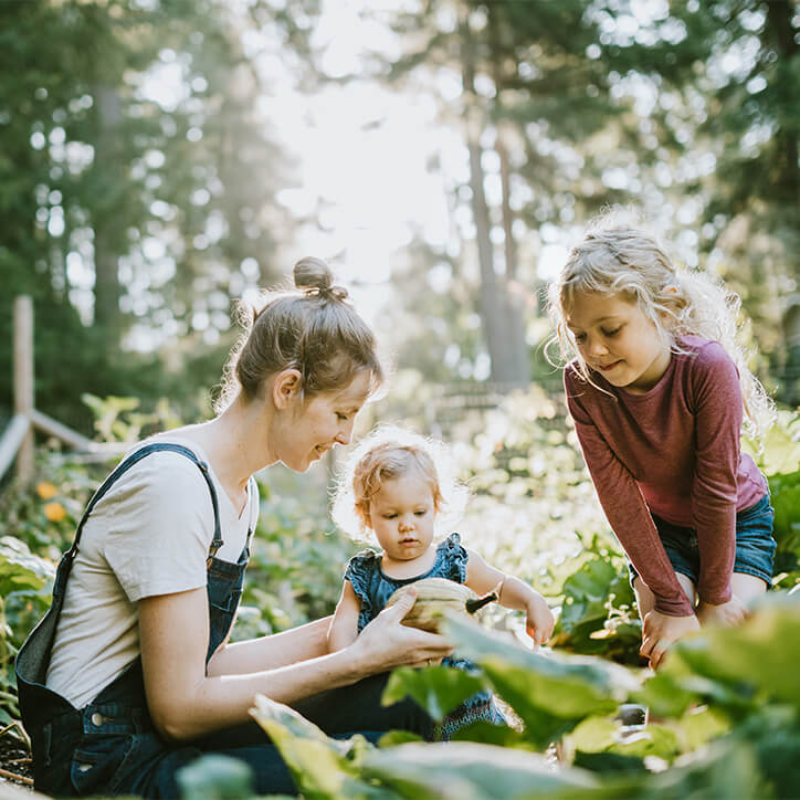 Eine Mutter mit ihren Kindern im Garten bei einem nährstoffreichen Picknick.