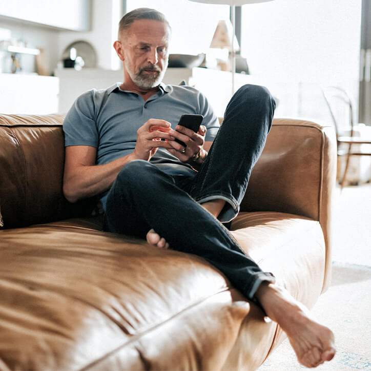 Mann mit Handy sitzt auf Ledersofa