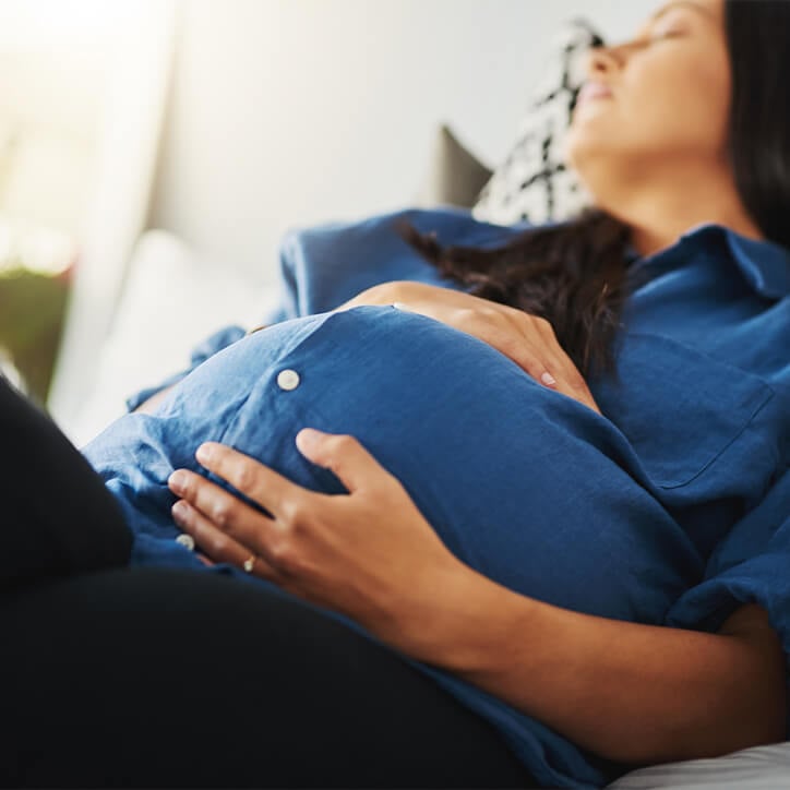 Schwangere Frau liegt mit geschlossenen Augen auf Sofa