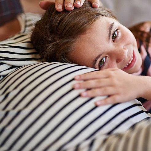 Kind legt Kopf auf Babybauch der Mutter